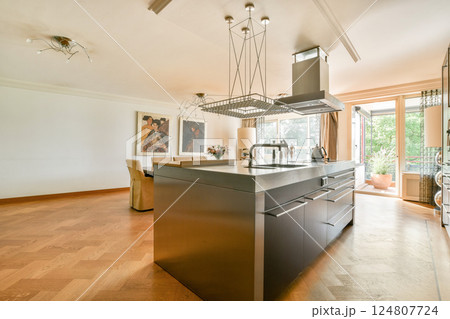 A sleek modern kitchen featuring stylish cabinets, a central island, and large windows that allow natural light to fill the space, enhancing its contemporary design. 124807724