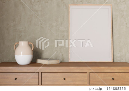 A minimalist interior showcases an empty picture frame on a wooden console, accompanied by a decorative vase and book. This setup invites personal artistic expression and creativity. 3D render. 124808336