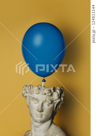 antique statue of a young man on a yellow background with a blue balloon 124811144