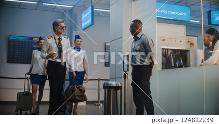 Airport Terminal: Airline Pilot and Two Flight Attendants Walking, Passing by Security Officer 124812239