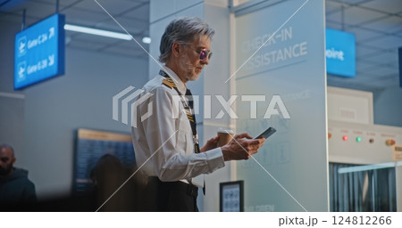 Airline Pilot Using Smartphone, Waiting for Commercial Flight in Airline Hub Lounge Airline Pilot Using Smartphone, Waiting for Commercial Flight in Airline Hub Lounge 124812266