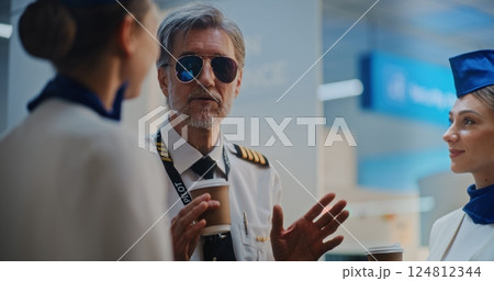 Airline Captain in Glasses Talking to Two Beautiful Stewardesses in Airport Terminal 124812344