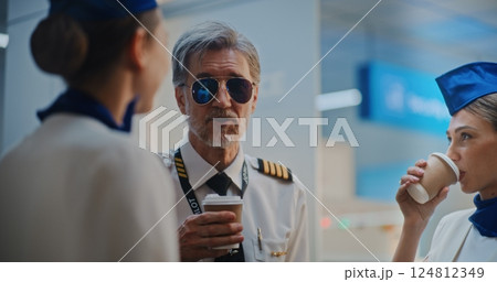 Airline Captain in Glasses Talking to Two Beautiful Stewardesses in Airport Terminal 124812349