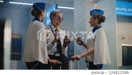 Crowded Airport Terminal: Airline Captain and Two Beautiful Stewardesses Talking, Waiting for Flight 124812399