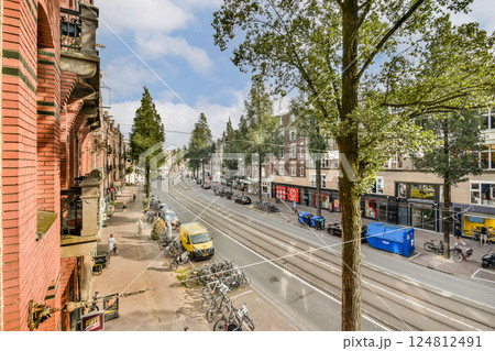 A picturesque urban street scene featuring lush trees lining the road, shops along the sidewalk, and vehicles parked in a lively neighborhood. A picturesque urban street scene featuring lush trees lining the road, shops along the sidewalk, and vehicles parked in a lively neighborhood. 124812491