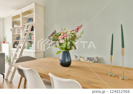 A cozy dining area featuring a wooden table, white chairs, and a lovely bouquet of flowers set against a stylish backdrop. A cozy dining area featuring a wooden table, white chairs, and a lovely bouquet of flowers set against a stylish backdrop. 124812568