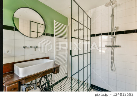 A stylish bathroom featuring a glass shower, classic sink, and chic decor. The combination of green walls and intricate tile patterns enhance the modern aesthetic. 124812582