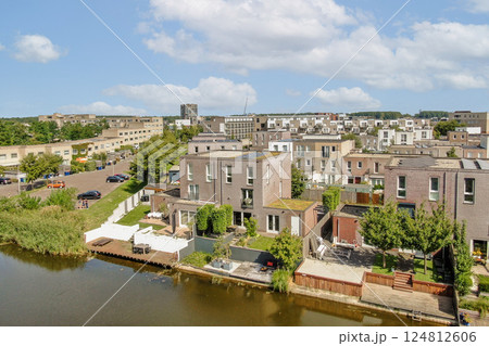 Aerial view showcasing contemporary houses beside a tranquil waterway, enhanced by lush greenery and clear blue skies, exemplifying urban living in harmony with nature. 124812606