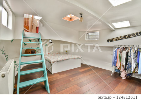 A cozy interior featuring a small room with a wooden floor, a spiral staircase, and neatly hung clothes. It exudes minimalism and comfort. 124812611