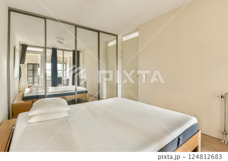 A sleek and contemporary bedroom featuring a minimalist design, mirrored wardrobes, and natural light illuminating the space. Perfect for modern living. 124812683