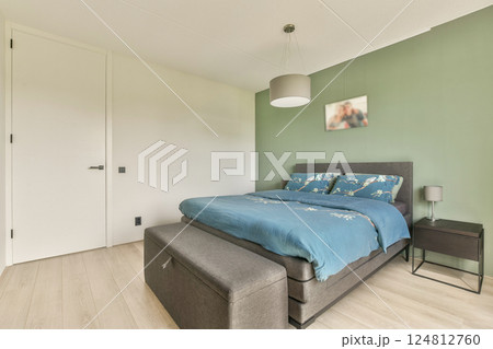 A stylish modern bedroom featuring a cozy bed dressed in blue linens, a minimalist design, and calming green wall accents, perfect for relaxation. A stylish modern bedroom featuring a cozy bed dressed in blue linens, a minimalist design, and calming green wall accents, perfect for relaxation. 124812760