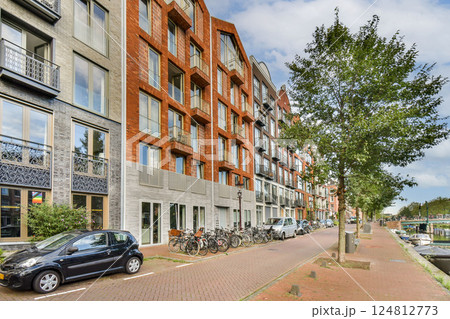A vibrant urban scene featuring modern buildings along a tree-lined street with parked vehicles, showcasing contemporary architecture and greenery. A vibrant urban scene featuring modern buildings along a tree-lined street with parked vehicles, showcasing contemporary architecture and greenery. 124812773