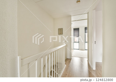 This image showcases a bright and modern hallway with white walls and wooden flooring, leading to a spacious area. Natural light floods through large windows. 124812800