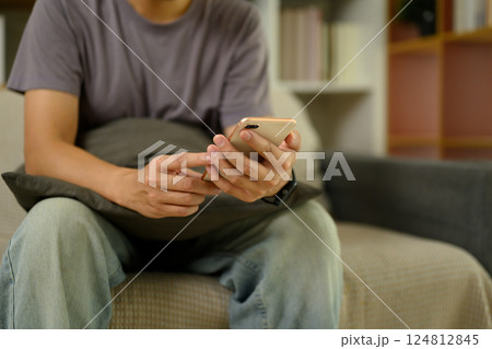 Cropped shot man in casual clothes using mobile phone on couch at home Cropped shot man in casual clothes using mobile phone on couch at home 124812845