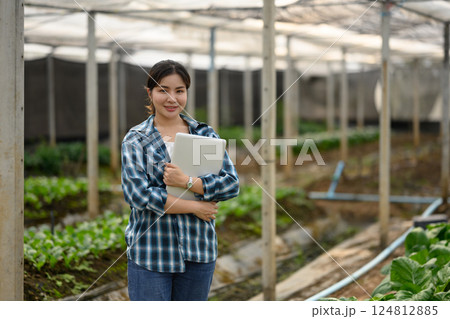Portrait of confident female farmer holding laptop standing in organic farm 124812885
