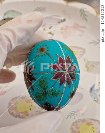 Traditional Ukrainian pysanka crafted using beeswax technique to create intricate folk patterns on an Easter egg with vibrant turquoise and red colors 124813012