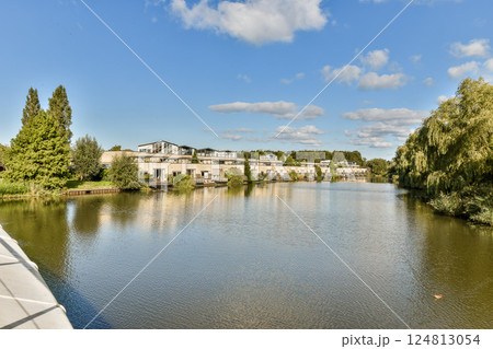 A picturesque scene featuring a calm river lined with modern residences and lush greenery under a clear blue sky, creating a serene atmosphere. A picturesque scene featuring a calm river lined with modern residences and lush greenery under a clear blue sky, creating a serene atmosphere. 124813054