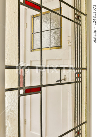 A beautifully crafted stained glass panel featuring intricate patterns in red and gold, framing a white door. The colorful glass catches the light artistically. 124813073