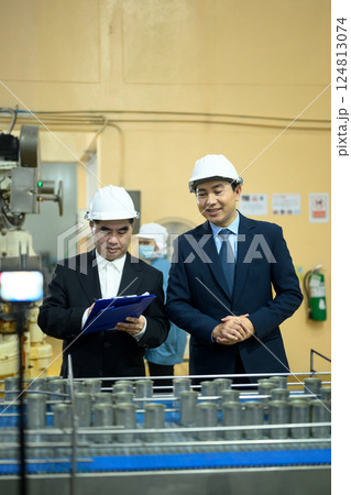 Factory supervisors in safety helmets examining a conveyor belt with metal cans in production plant 124813074