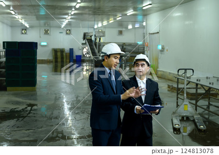 Two factory managers in hard hats discussing production plans inside a manufacturing facility 124813078