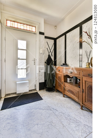 A stylish entrance hall featuring a sleek door, marble flooring, and a wooden console with decorative elements, creating an inviting atmosphere. 124813080