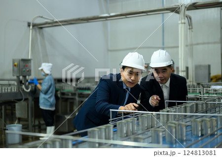 Two factory managers wearing hard hats inspecting a production line in an industrial facility 124813081
