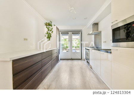 A bright and modern kitchen featuring a minimalist design, sleek cabinets, and large windows that invite natural light into the space. 124813304