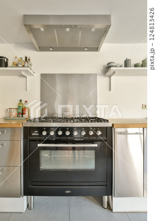 A contemporary kitchen featuring a black gas stove, stainless steel appliances, and minimalistic cabinetry. Ideal for culinary enthusiasts and modern design lovers. 124813426