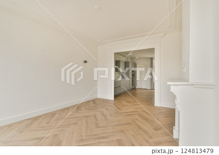 A spacious, modern interior featuring neutral walls and a herringbone-patterned wooden floor, showcasing minimalist aesthetics and elegant furnishings. 124813479