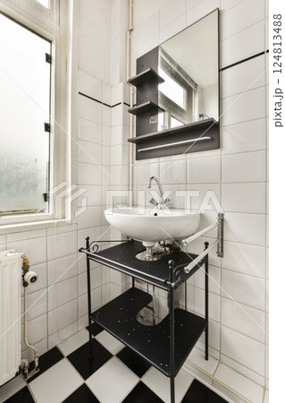 A stylish bathroom featuring a sleek sink, modern mirror, and functional shelving. The space is adorned with black and white tiles, enhancing its contemporary design. 124813488