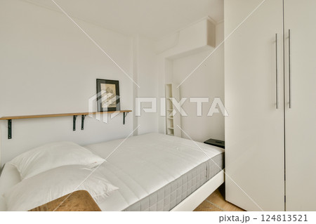 A simple and modern bedroom featuring a bed with white linens, a shelf, and clean lines that create a serene atmosphere. 124813521