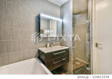 A sleek and contemporary bathroom showcasing minimalist design elements, featuring gray tiles, a rectangular mirror, and a stylish vanity with storage. 124813539