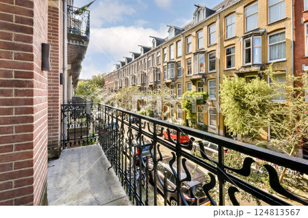 A picturesque view from a balcony overlooking a tree-lined street and elegant buildings with detailed architecture, showcasing urban life. 124813567