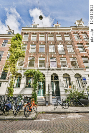 A picturesque view of a street in Amsterdam featuring bicycles lined up against a charming building adorned with lush greenery. The scene captures urban tranquility. 124813613