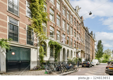 A charming street in Amsterdam featuring lush greenery, traditional architecture, and parked bicycles, embodying the city's unique culture and lifestyle. 124813651