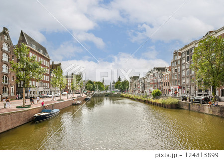 A charming view of a canal surrounded by traditional Dutch architecture and lush green trees, perfect for capturing the essence of Amsterdam's beauty. 124813899