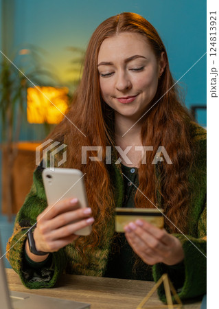 Smiling woman using bank credit card and smartphone for online shopping payments at home office Smiling woman using bank credit card and smartphone for online shopping payments at home office 124813921