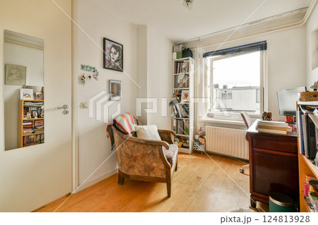 A serene room featuring a comfortable chair, a bookshelf filled with books, and a large window letting in natural light, creating an inviting atmosphere. A serene room featuring a comfortable chair, a bookshelf filled with books, and a large window letting in natural light, creating an inviting atmosphere. 124813928