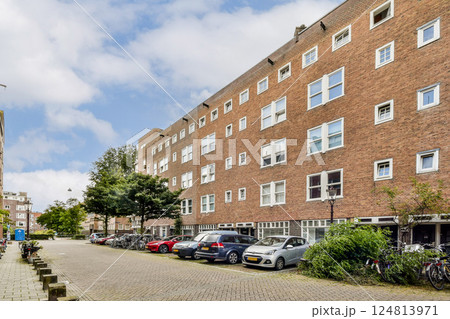A scenic view of a quiet urban street lined with modern residential buildings, trees, and parked cars, showcasing a blend of nature and city life. 124813971