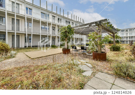 A modern residential building featuring green landscaping, outdoor seating areas, and a serene pathway for relaxation and leisure activities. A modern residential building featuring green landscaping, outdoor seating areas, and a serene pathway for relaxation and leisure activities. 124814026