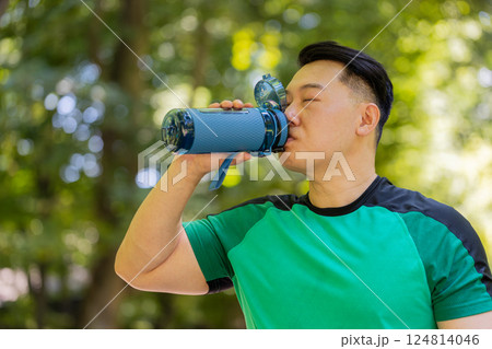 Sporty athletic thirsty Chinese Asian sportsman runner jogger drinking water after workout in park 124814046