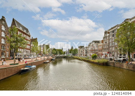 A beautiful perspective of Amsterdam showcasing its iconic canal, historic buildings, and lush trees under a blue sky, reflecting the city's charm and serenity. A beautiful perspective of Amsterdam showcasing its iconic canal, historic buildings, and lush trees under a blue sky, reflecting the city's charm and serenity. 124814094