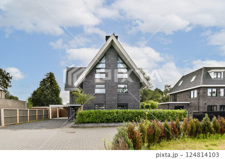 A contemporary architectural design showcases a striking house amidst vibrant landscaping and trees, reflecting elegance and style in residential living. A contemporary architectural design showcases a striking house amidst vibrant landscaping and trees, reflecting elegance and style in residential living. 124814103