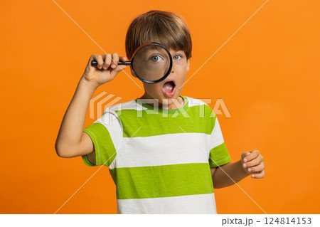 Child boy kid holds magnifying glass near face looking at camera with big zoomed eye, analyzing 124814153