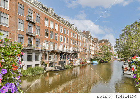 A picturesque scene of traditional Dutch architecture lining a serene canal, adorned with vibrant flowers and a clear blue sky above. 124814154