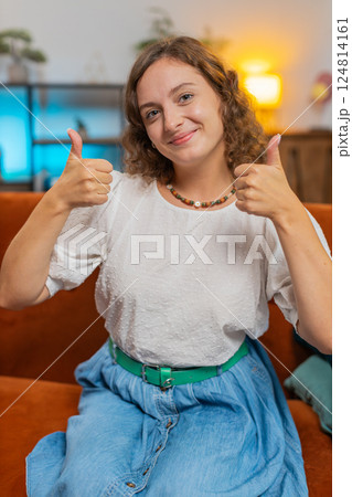Portrait of excited smiling Caucasian woman showing double thumbs up sitting on sofa couch at home Portrait of excited smiling Caucasian woman showing double thumbs up sitting on sofa couch at home 124814161