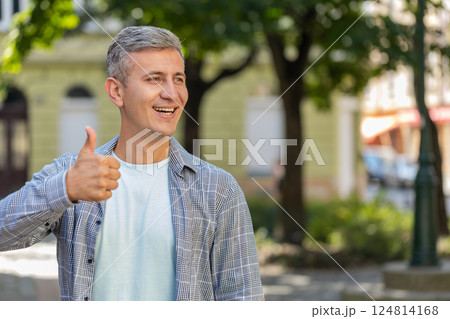 Happy mature man showing thumbs up agrees giving positive reply recommends good idea on city street Happy mature man showing thumbs up agrees giving positive reply recommends good idea on city street 124814168