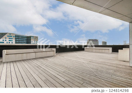 A sleek outdoor area showcasing modern architecture, blending lines and textures. The vast wooden deck is complemented by contemporary buildings and a clear sky. 124814298
