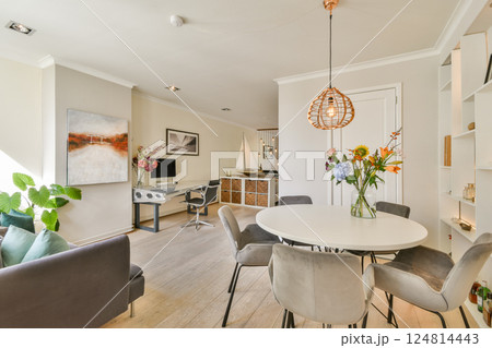 Stylish living area featuring a round table, comfortable chairs, and a blend of natural and artificial lighting. Elegant decor elements create a welcoming ambiance. 124814443