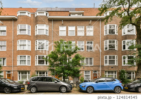 A picturesque urban scene featuring a classic apartment building surrounded by lush trees and parked cars, showcasing modern city life and architecture. 124814545